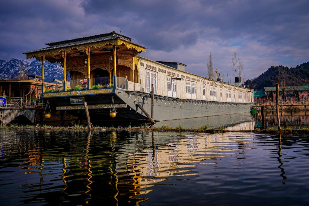 Scenic view of a traditional houseboat on Dal Lake, Srinagar under a vivid sky reflecting in calm waters.