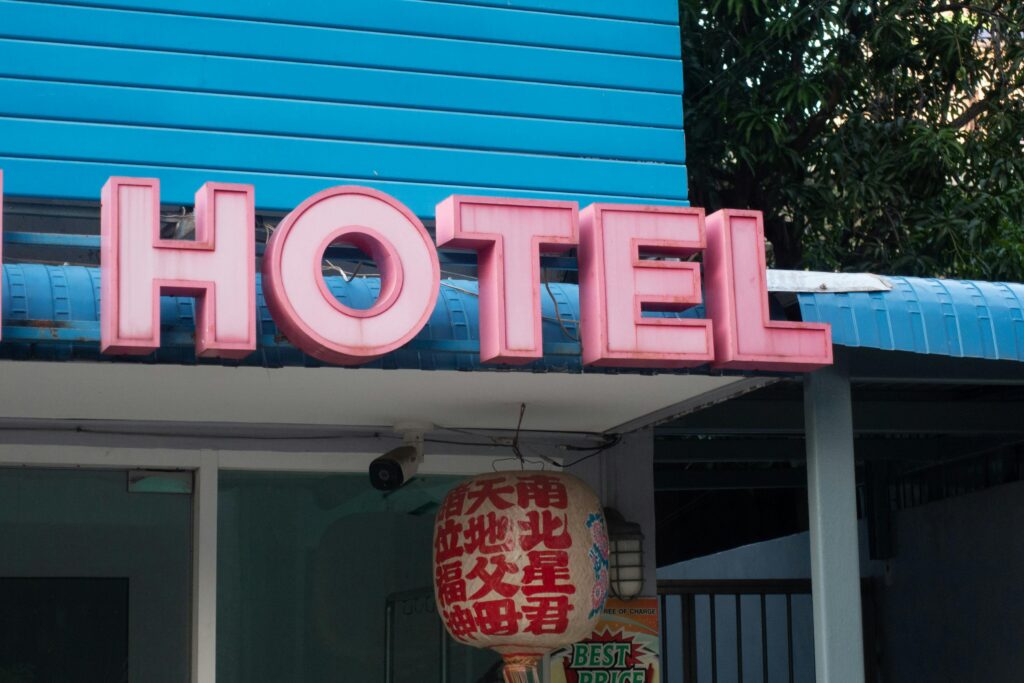 Vibrant pink hotel sign attached to a building with a blue wall background, featuring a Chinese lantern.