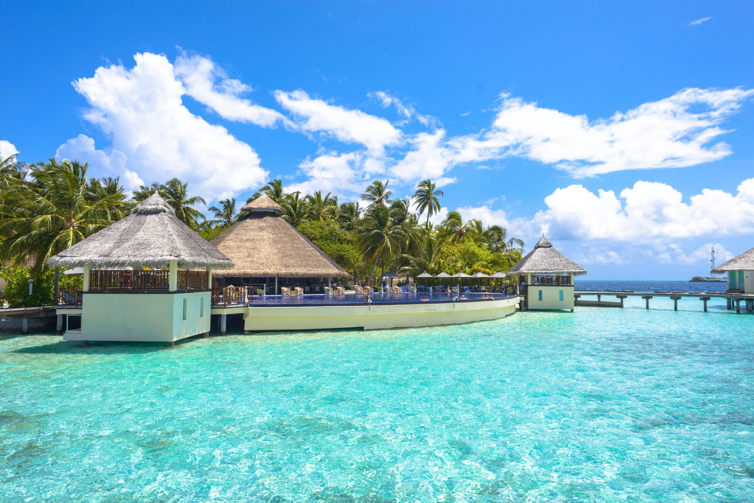 Stunning view of a tropical resort in the Maldives with clear turquoise waters and lush palm trees.